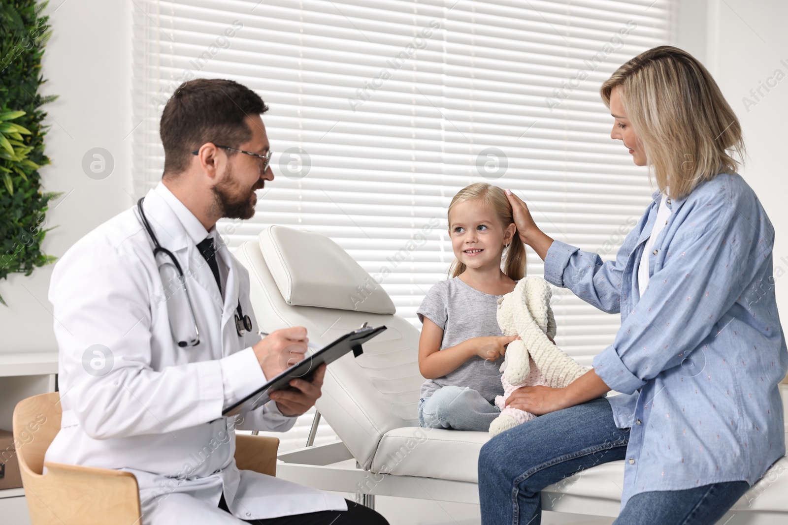 Photo of Doctor consulting little girl with toy and her mother in hospital