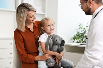 Doctor consulting little girl with toy and her mother in hospital