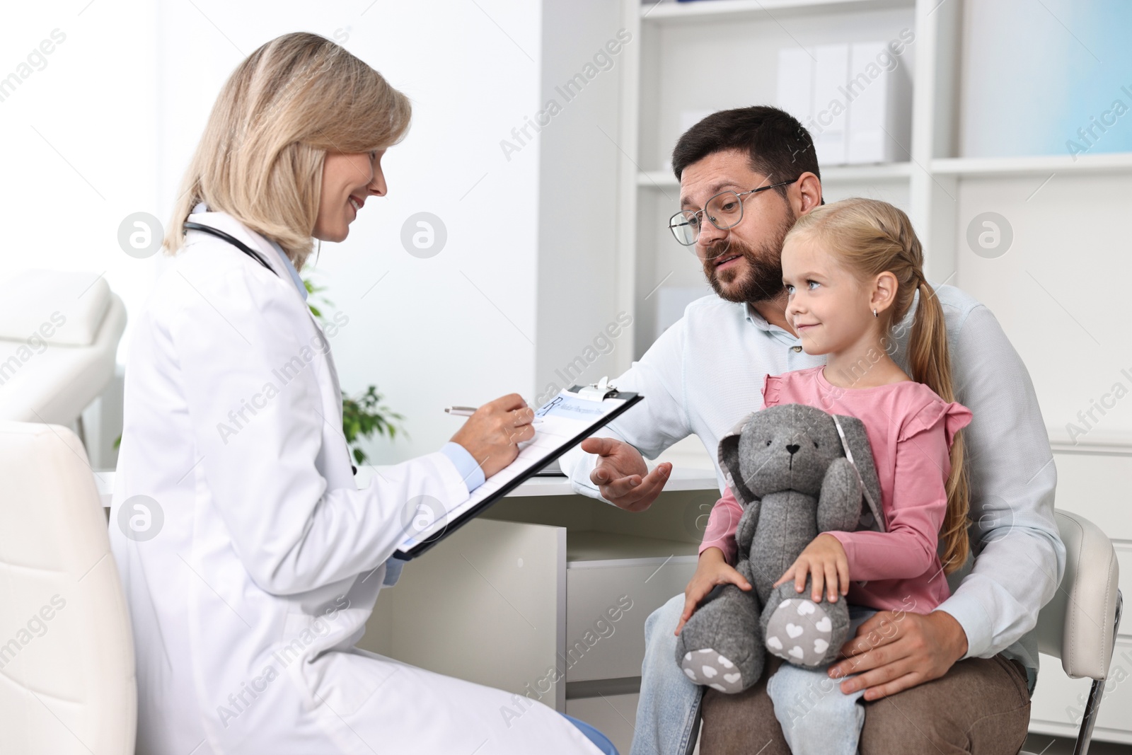 Photo of Doctor consulting little girl with toy and her father in hospital