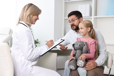 Doctor consulting little girl with toy and her father in hospital