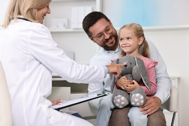 Doctor consulting little girl with toy and her father in hospital