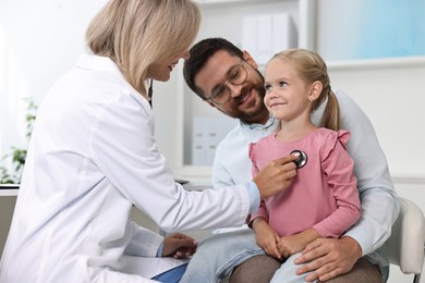 Doctor examining little girl with stethoscope and her father in hospital