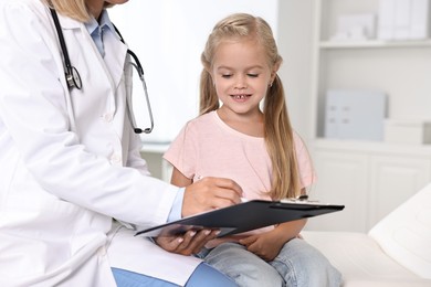 Doctor with clipboard consulting little girl in hospital, closeup