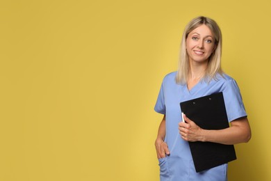 Portrait of nurse in medical uniform with clipboard on yellow background, space for text