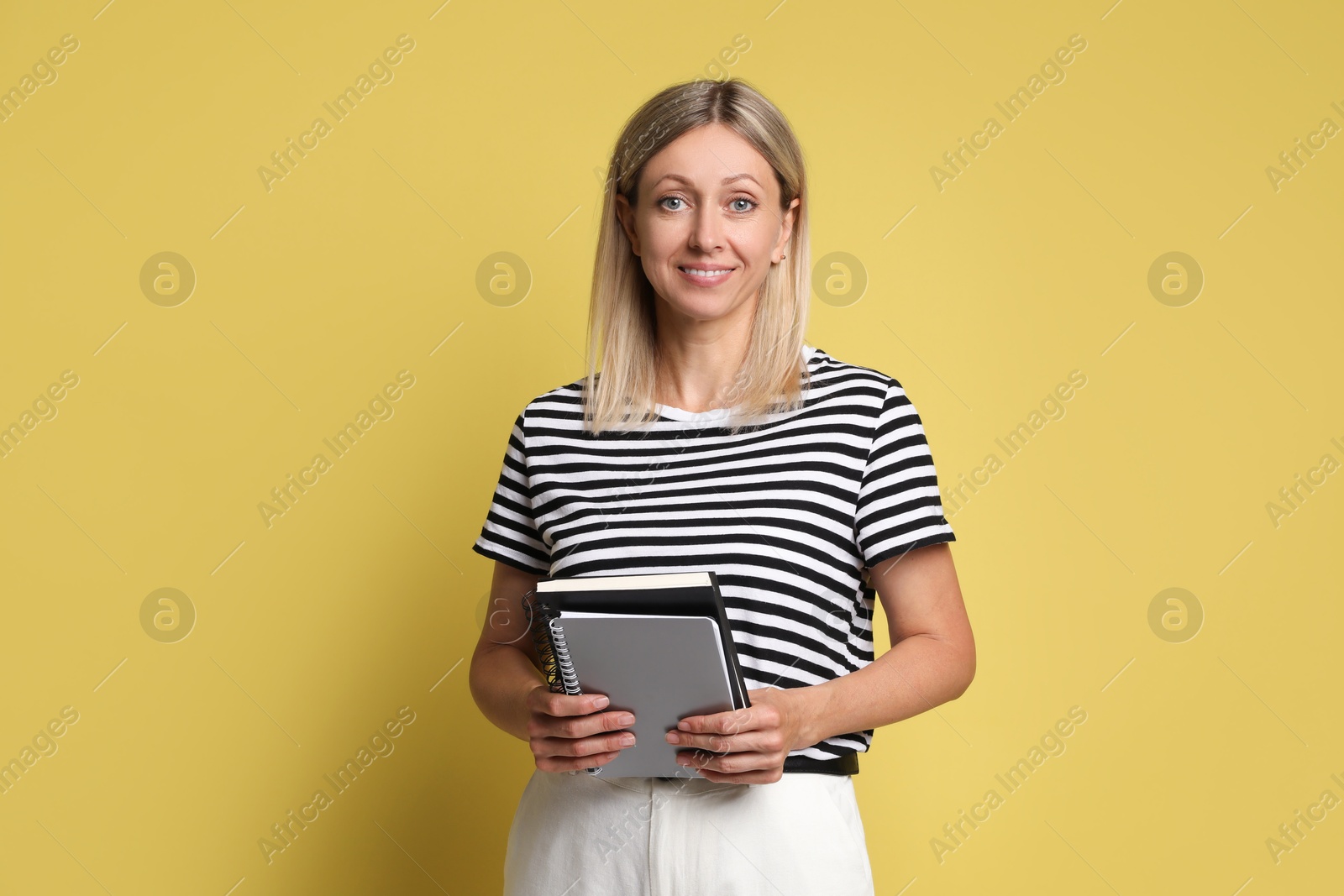 Photo of Beautiful smiling woman with notebooks on yellow background