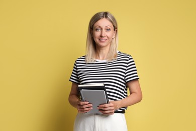 Beautiful smiling woman with notebooks on yellow background