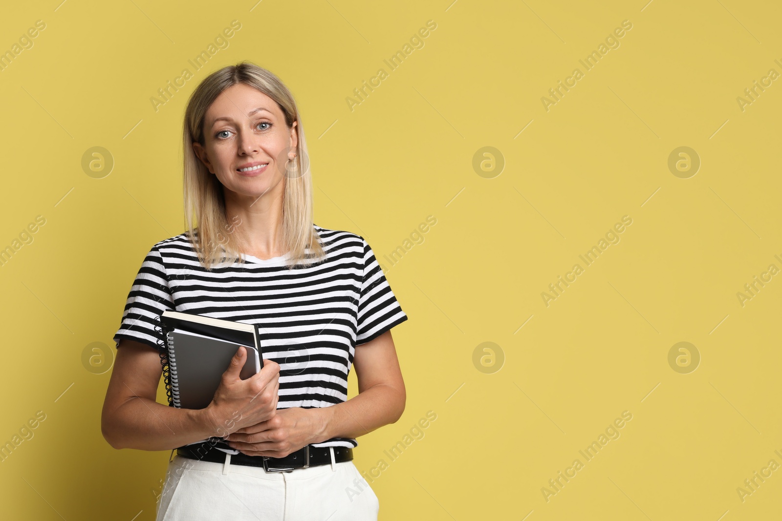 Photo of Beautiful smiling woman with notebooks on yellow background, space for text