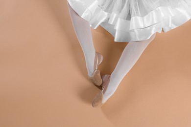 Little ballerina wearing pointe shoes on beige background, top view. Space for text