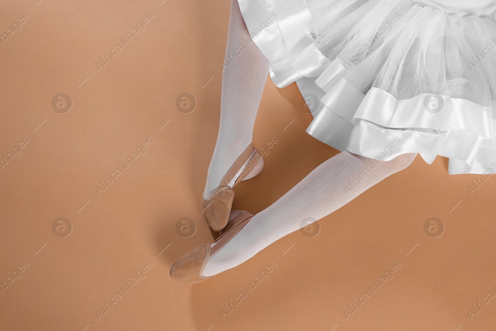 Photo of Little ballerina wearing pointe shoes on beige background, top view. Space for text