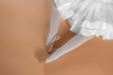 Little ballerina wearing pointe shoes on beige background, top view. Space for text