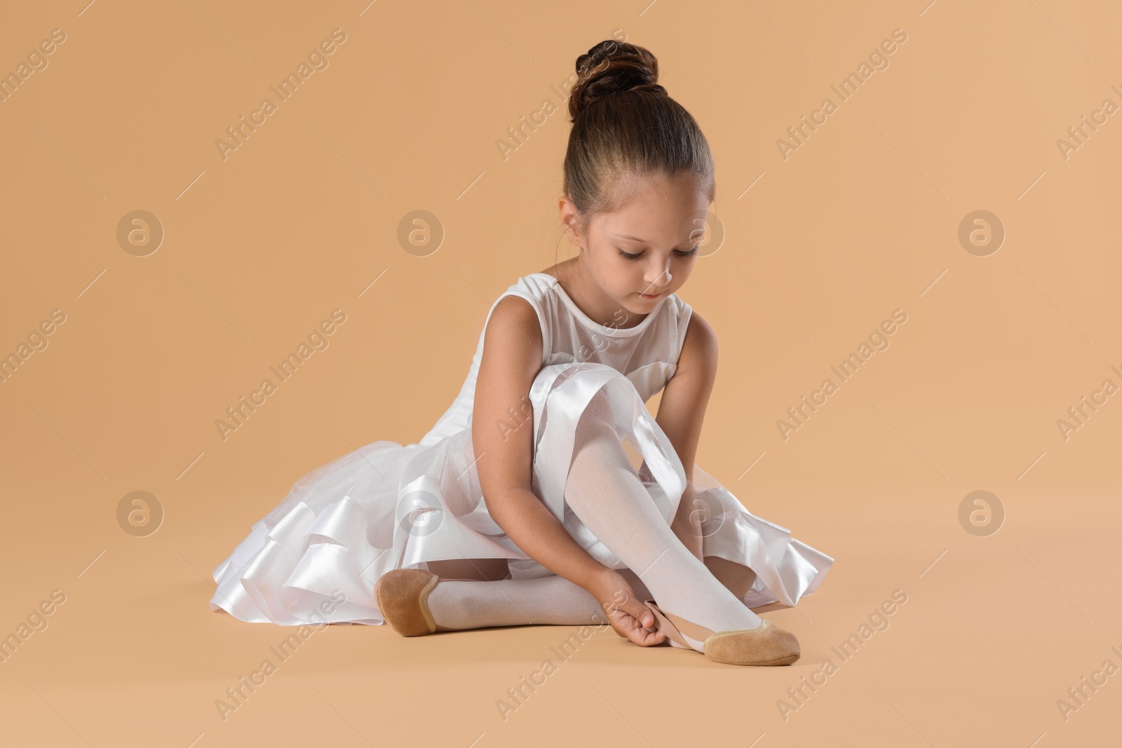 Photo of Little ballerina putting on pointe shoes against beige background