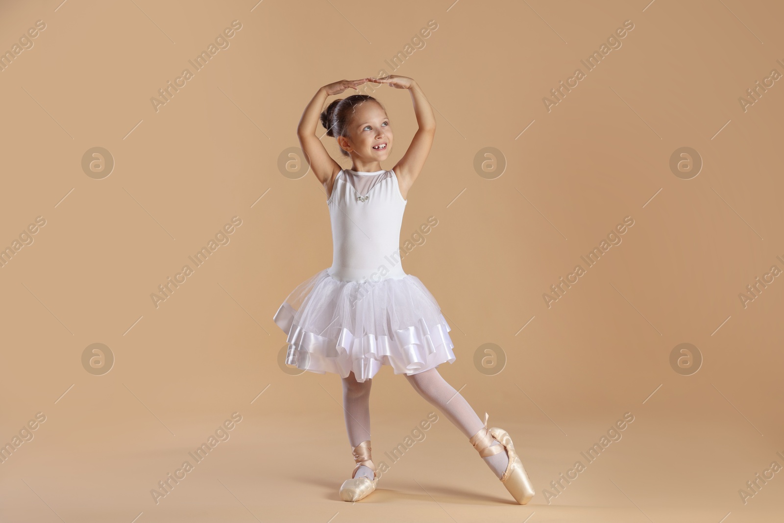 Photo of Little ballerina practicing dance moves on beige background