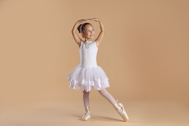 Little ballerina practicing dance moves on beige background