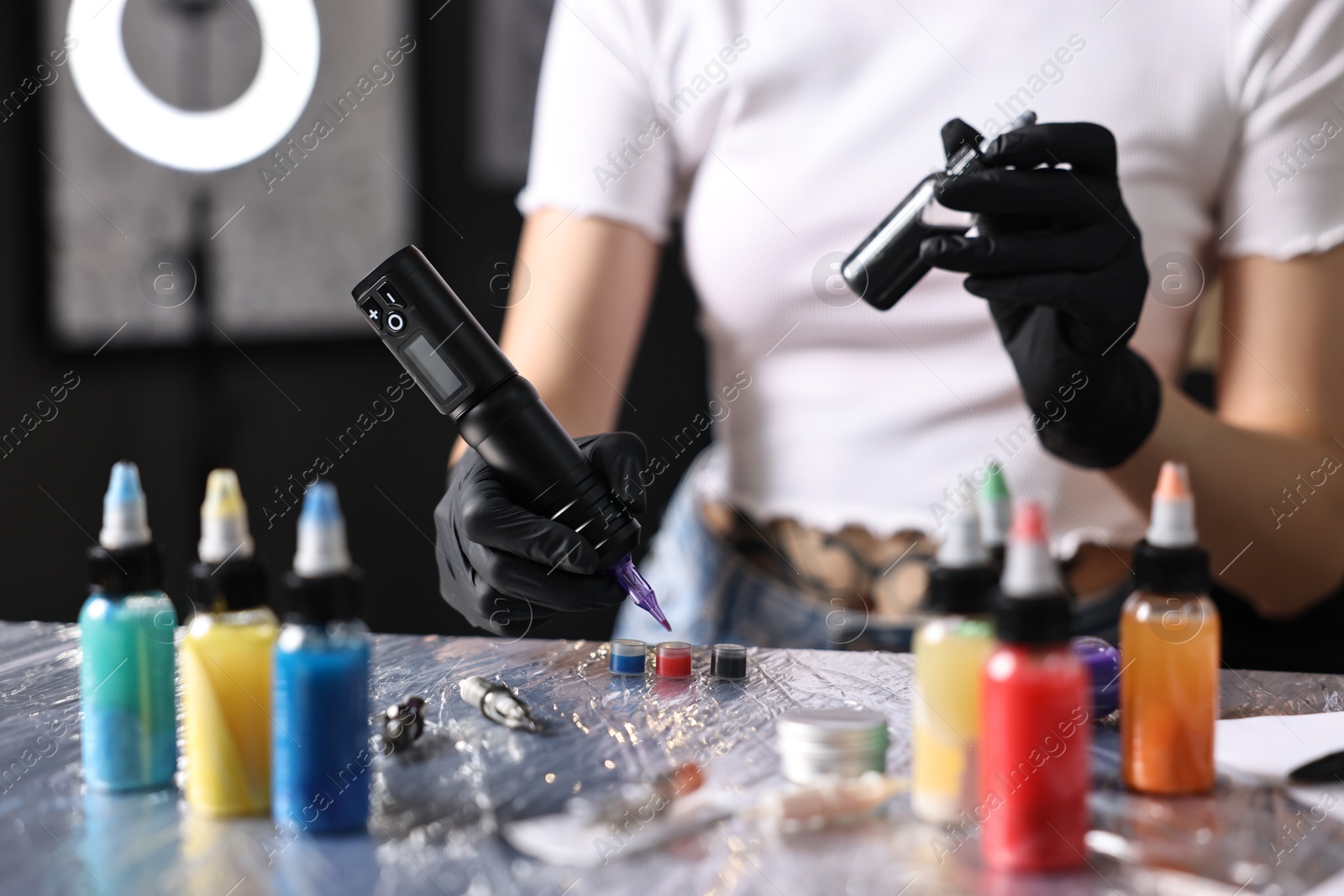 Photo of Professional artist working with tattoo machine and inks at sterile table in salon, closeup