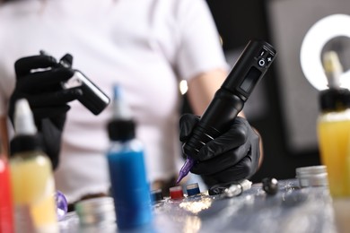 Photo of Professional artist working with tattoo machine and inks at sterile table in salon, closeup