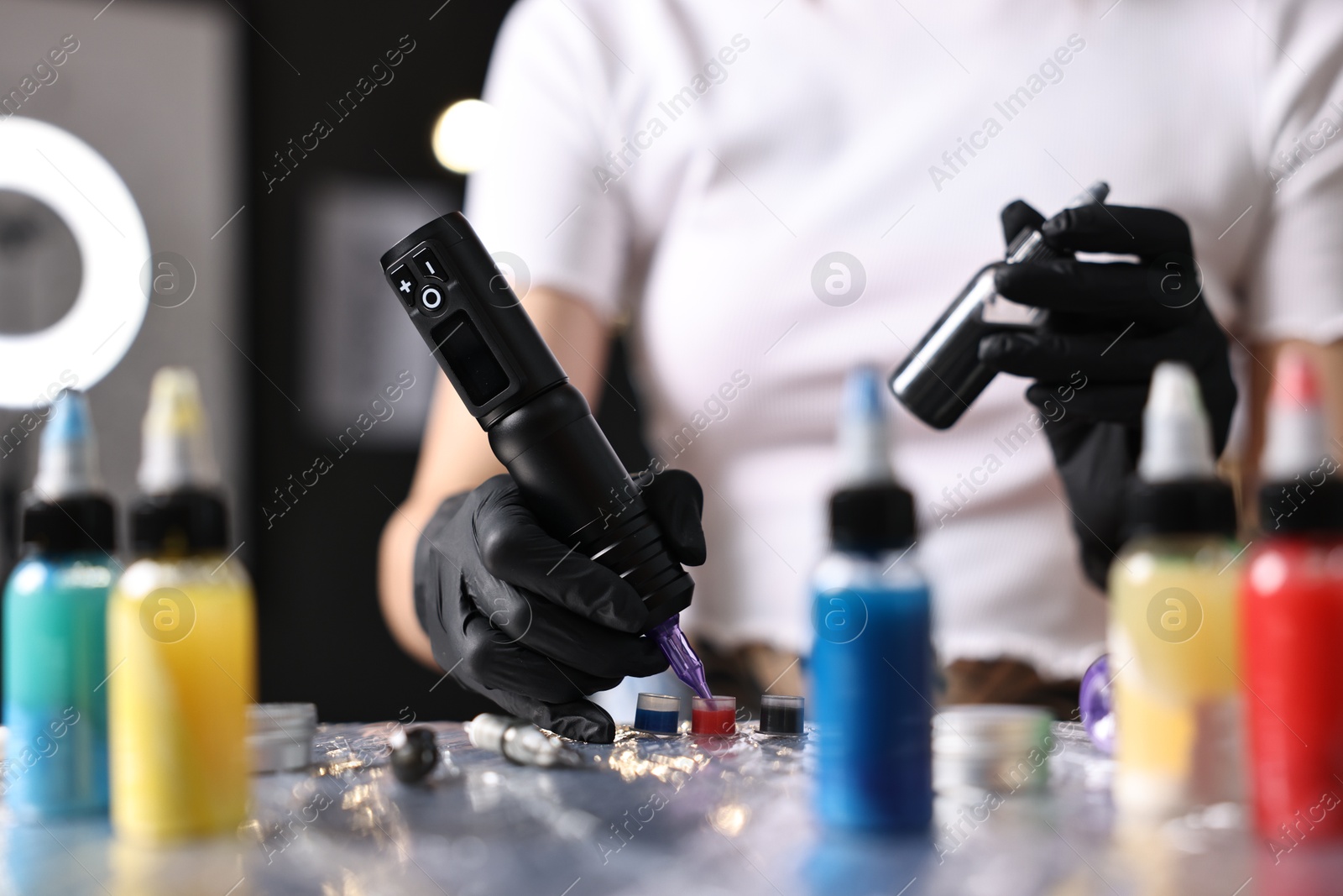 Photo of Professional artist working with tattoo machine and inks at sterile table in salon, closeup