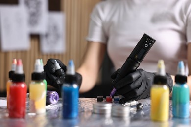 Professional artist working with tattoo machine and inks at sterile table in salon, closeup