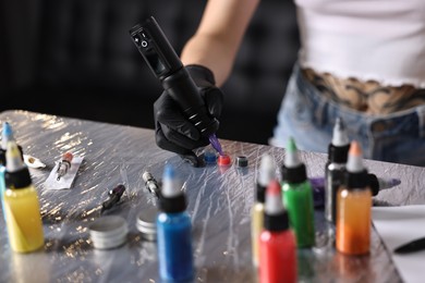 Photo of Professional artist working with tattoo machine and inks at sterile table in salon, closeup