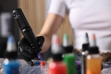 Photo of Professional artist working with tattoo machine and inks at sterile table in salon, closeup