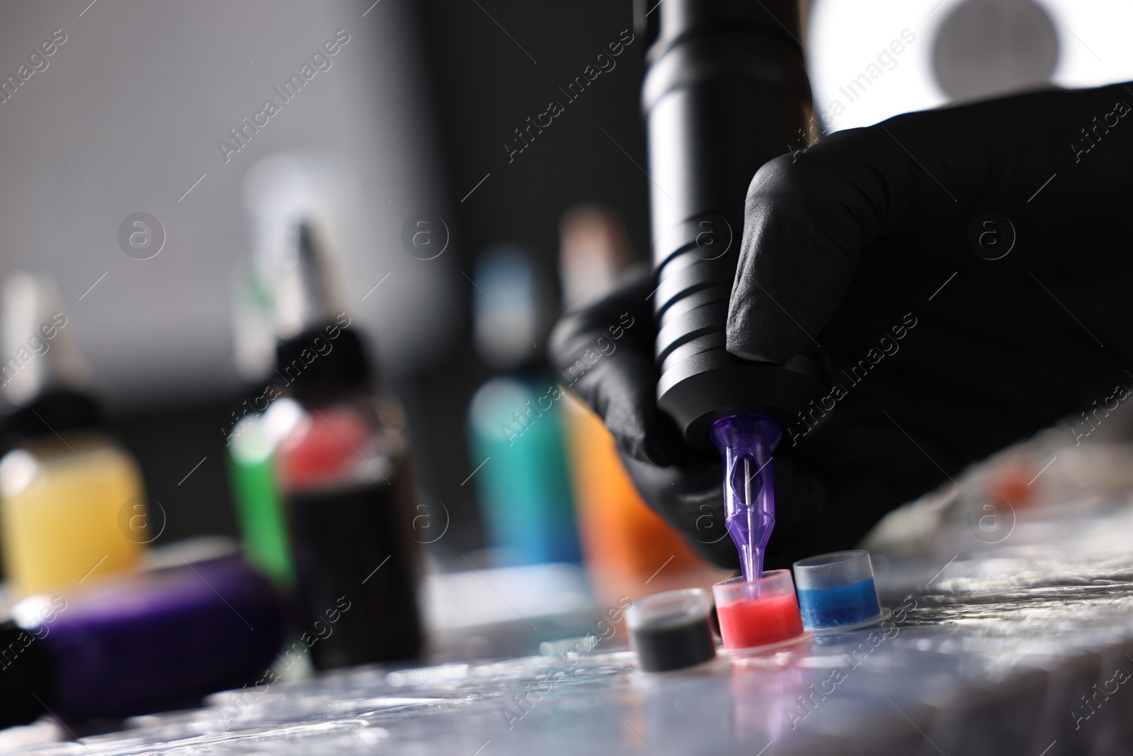 Photo of Professional artist working with tattoo machine and inks at sterile table in salon, closeup