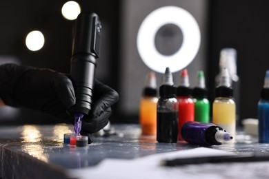 Photo of Professional artist working with tattoo machine and inks at sterile table in salon, closeup