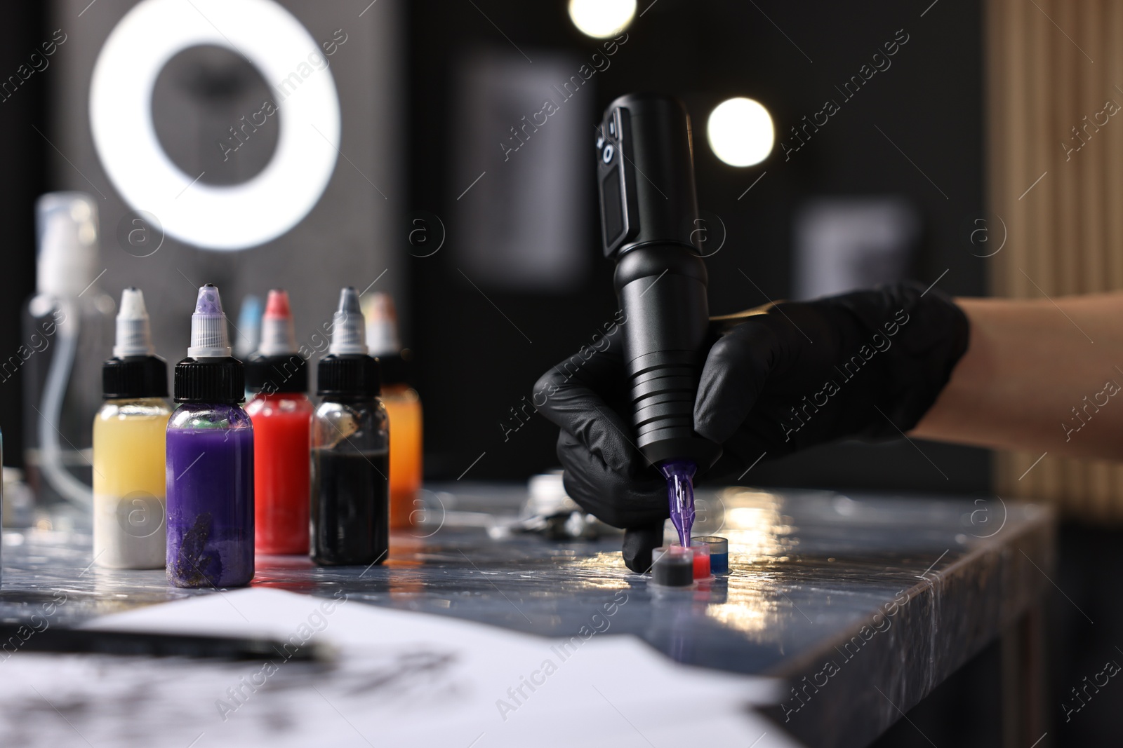 Photo of Professional artist working with tattoo machine and inks at sterile table in salon, closeup