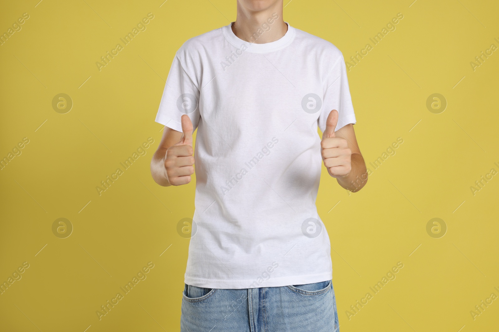 Photo of Teenage boy wearing white t-shirt and showing thumbs up on yellow background, closeup