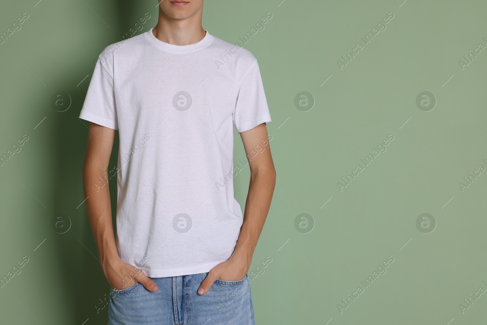 Photo of Teenage boy wearing white t-shirt on green background, closeup. Space for text