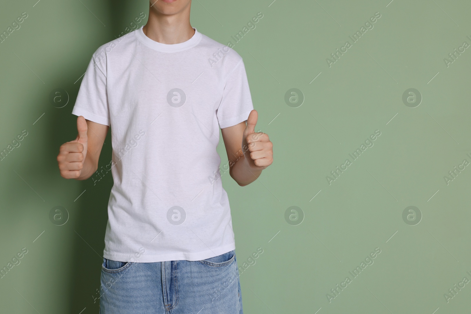 Photo of Teenage boy wearing white t-shirt and showing thumbs up on green background, closeup. Space for text