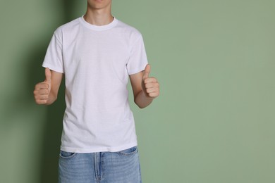 Photo of Teenage boy wearing white t-shirt and showing thumbs up on green background, closeup. Space for text