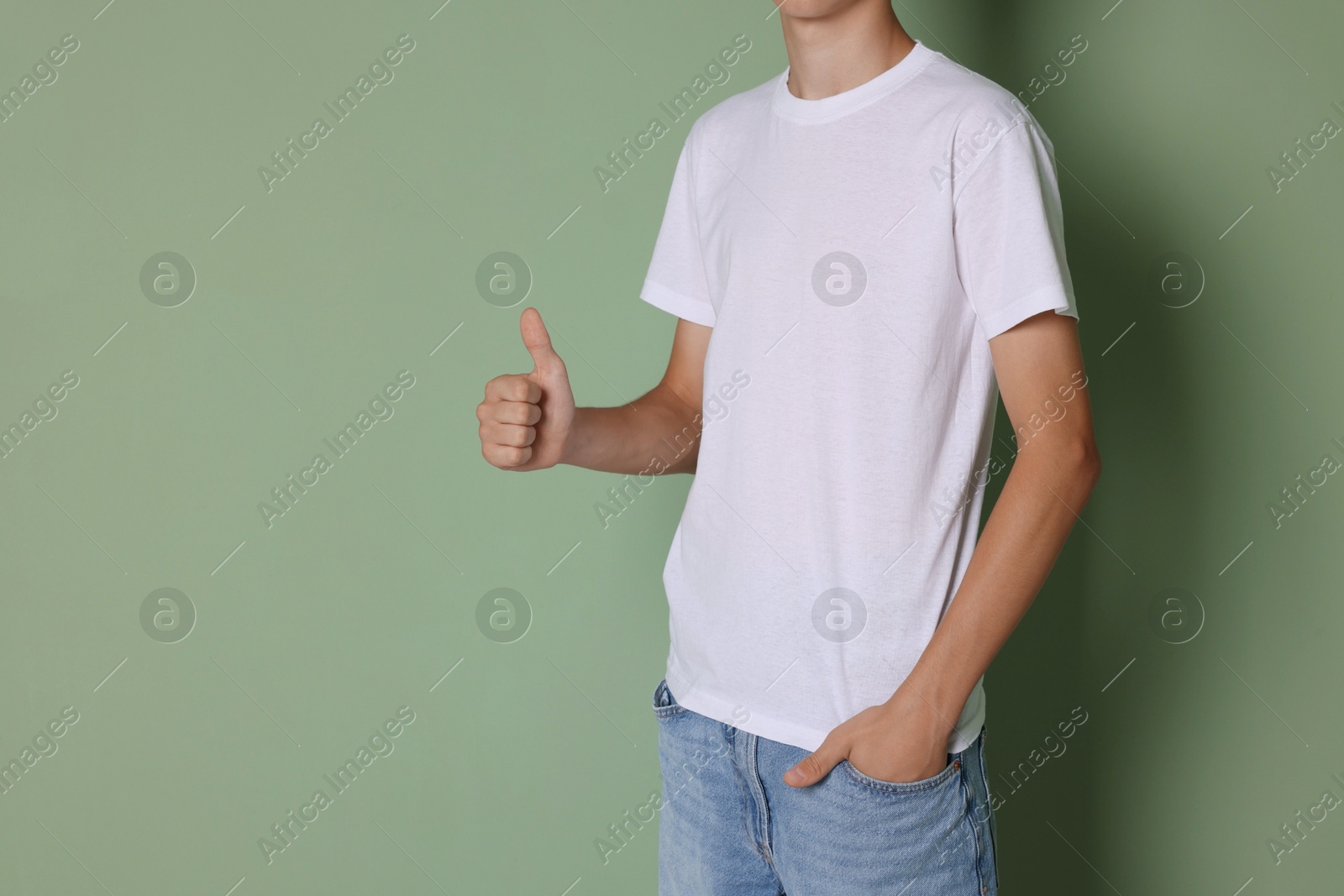 Photo of Teenage boy wearing white t-shirt and showing thumbs up on green background, closeup. Space for text