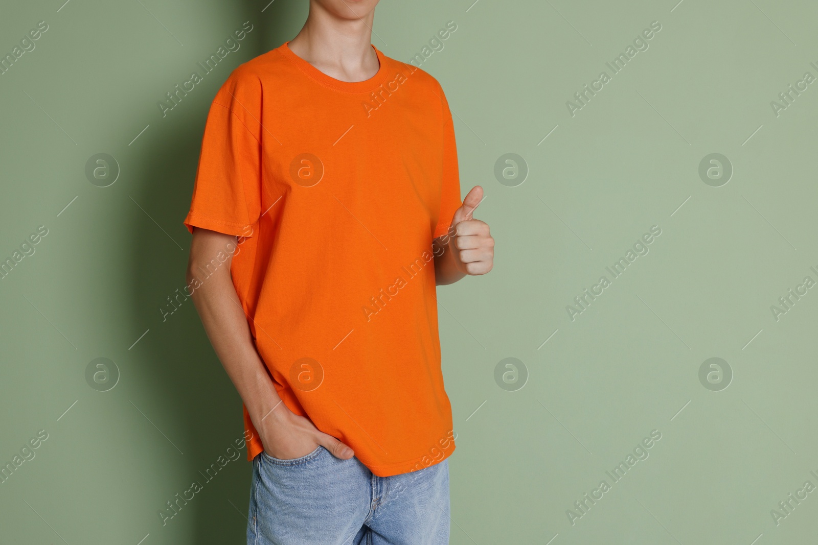 Photo of Teenage boy wearing orange t-shirt and showing thumbs up on green background, closeup. Space for text