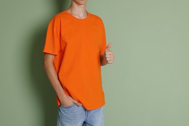 Teenage boy wearing orange t-shirt and showing thumbs up on green background, closeup. Space for text