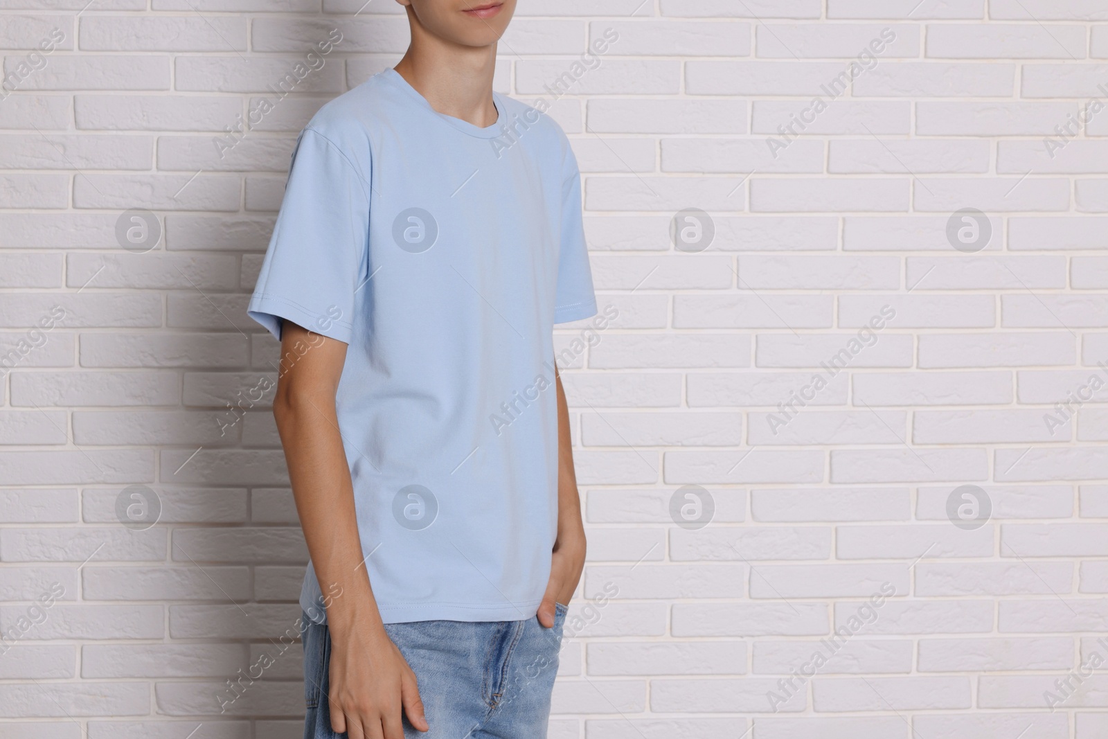 Photo of Teenage boy wearing light blue t-shirt near white brick wall, closeup. Space for text