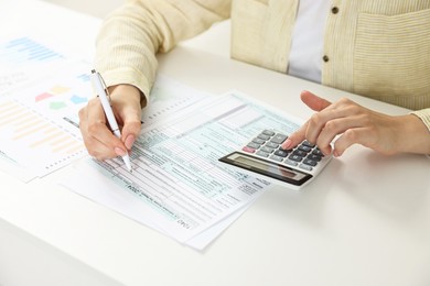 Budget planning. Woman with papers using calculator at white table, closeup