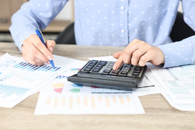 Photo of Budget planning. Woman with papers using calculator at wooden table, closeup