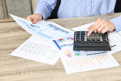 Budget planning. Woman with papers using calculator at wooden table, closeup