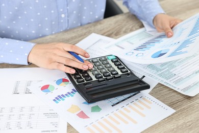 Photo of Budget planning. Woman with papers and calculator at wooden table, closeup