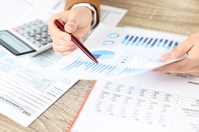 Budget planning. Woman with papers and calculator at wooden table, closeup