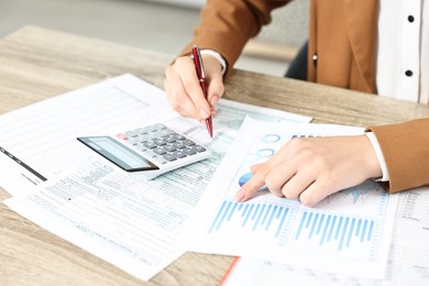 Photo of Budget planning. Woman with papers and calculator at wooden table, closeup