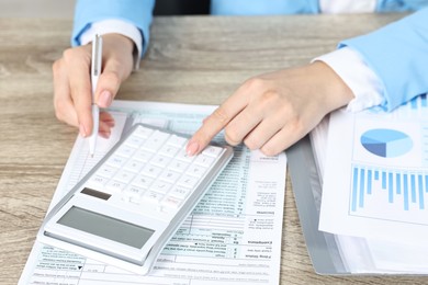 Photo of Budget planning. Woman with papers and calculator at wooden table, closeup