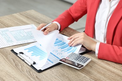 Budget planning. Woman with papers and calculator at wooden table, closeup