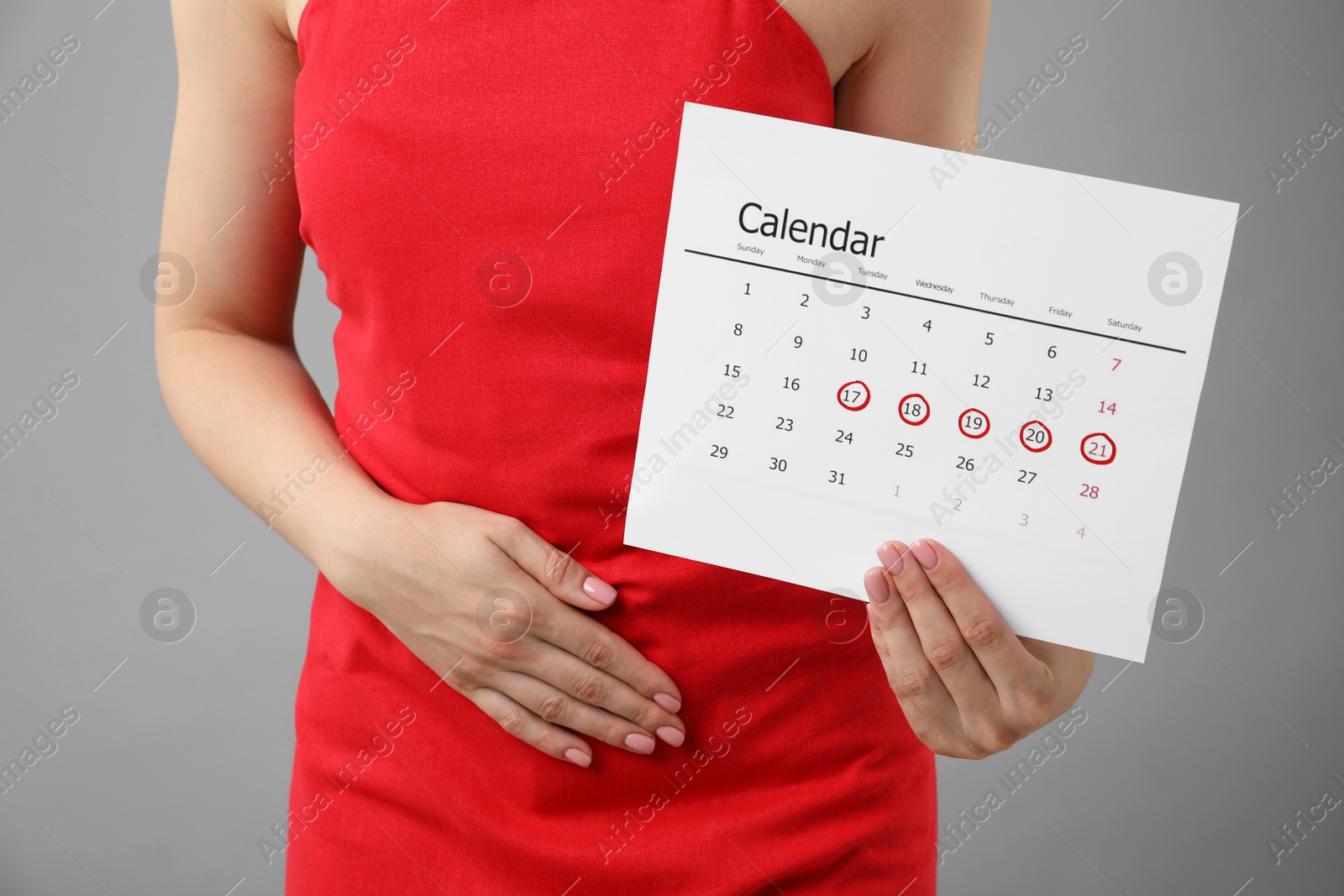 Photo of Woman holding calendar with marked menstrual cycle days and suffering from abdominal pain on grey background, closeup