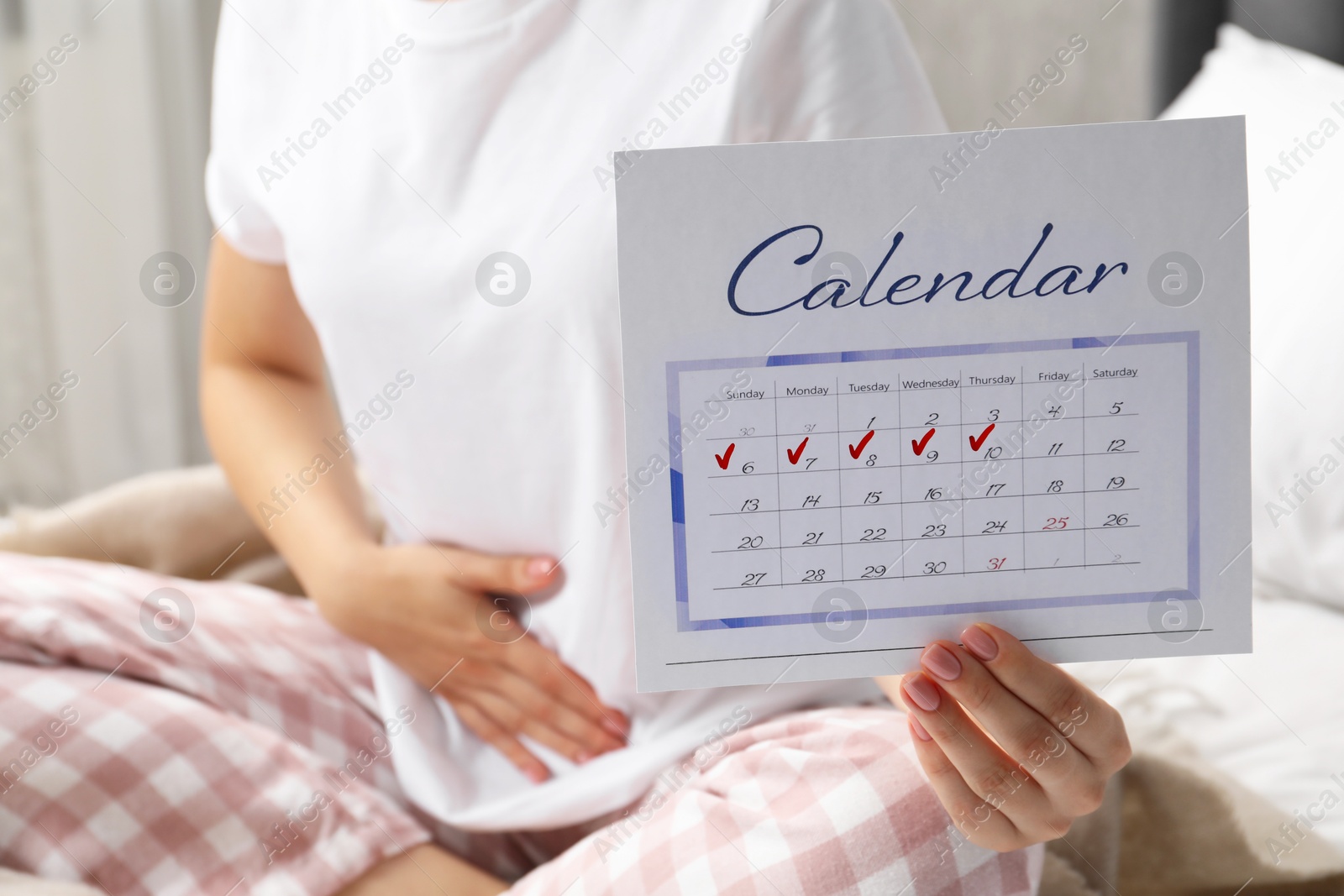 Photo of Woman holding calendar with marked menstrual cycle days on bed at home, closeup