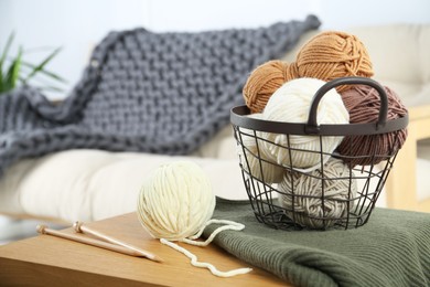 Photo of Basket with yarns, knitting needles and sweater on wooden table indoors