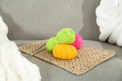 Photo of Skeins of soft yarn and knitting needles on sofa indoors