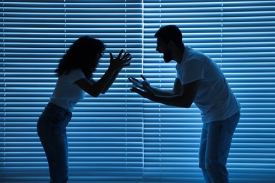 Photo of Emotional couple arguing indoors at night. Relationship problems