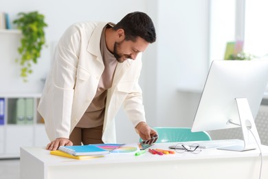 Photo of Designer with color samples working at table in office