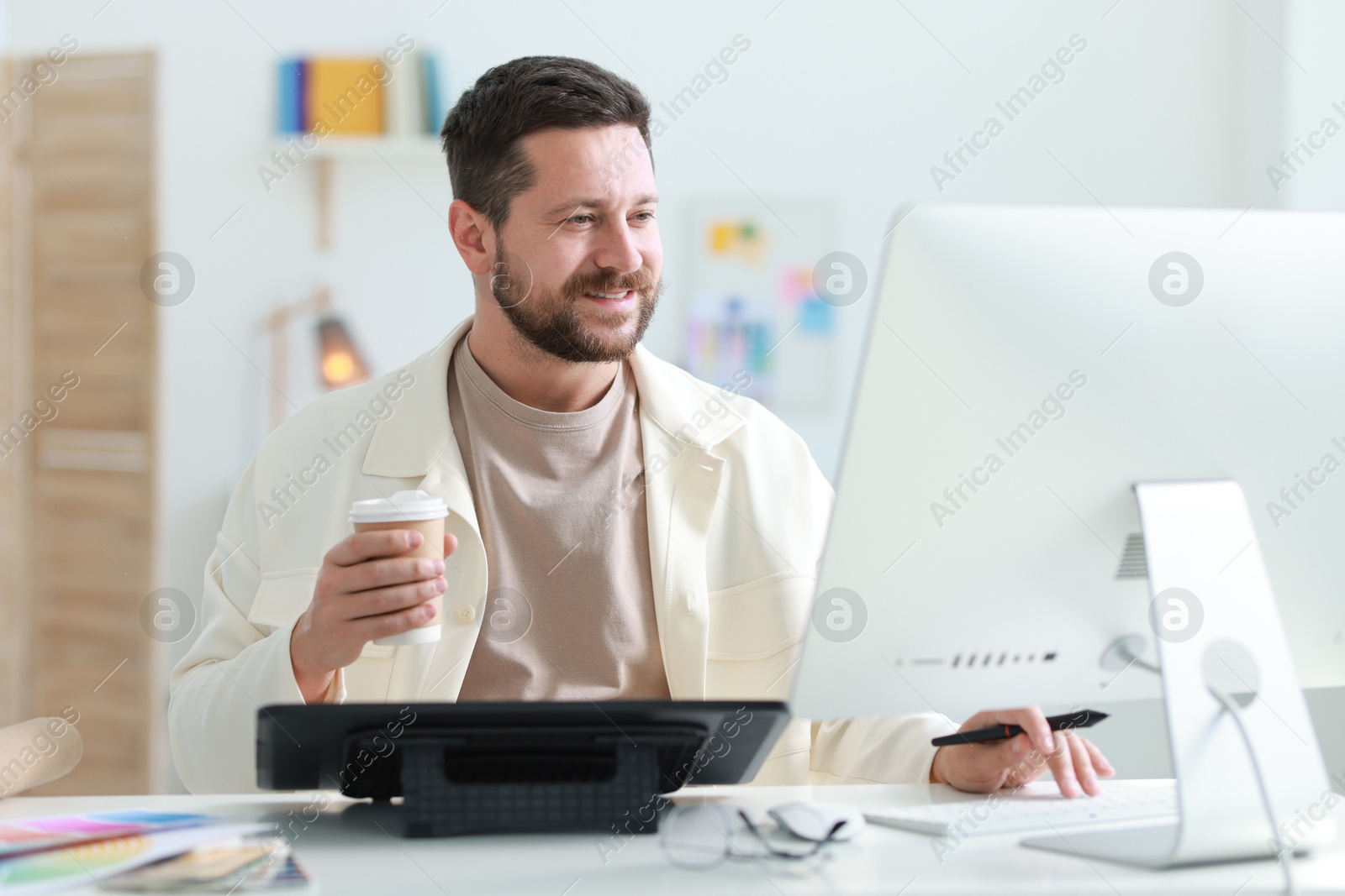 Photo of Designer with paper cup of drink working at table in office