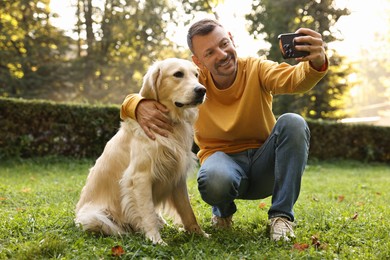 Photo of Smiling man with cute Golden Retriever dog taking selfie on spring day